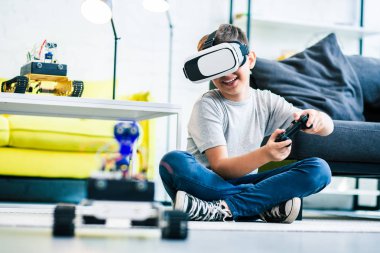 Bir uzaktan kumanda tutarak ve robotunu test ederken yerde oturan neşeli akıllı gülümseyen çocuk
