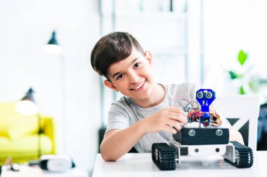 Neşeli akıllı öğrenci masada oturan ve evde bir robot cihaz inşa