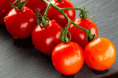 Olgun kırmızı kiraz domates dalı nın küçük damla su ve domates altında siyah kayrak yüzeyi ile fotoğraf kapatın