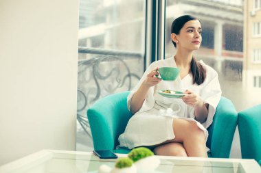 Bornozla huzurlu kadın uzağa bakıyor ve çay içiyor