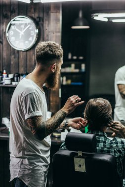 Calm careful barber working with his client and putting one hand up while looking at the reflection in the mirror
