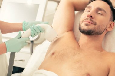 Profesyonel doktor koltuk altından kılçıkarırken gözleri kapalı ve gülümseyerek yatan genç sakin bir adamın yakın fotoğrafı