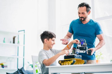 Mühendislik projesinde oğluna yardım ederken robot iktisadi bir cihaz tutan neşeli yetişkin adam