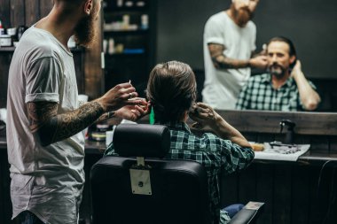 Careful bearded barber standing next to his client and touching his hair while making haircut