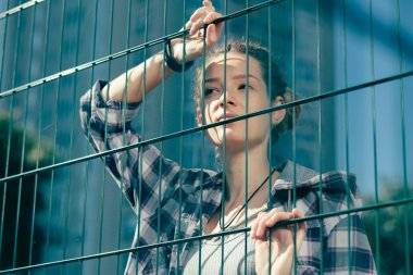 Sakin güzel genç kadın rahat giysiler giyen ve düşünceli zincir bağlantı çit eğilerek