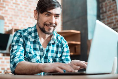 Modern serbest. Mutlu güzel hoş adam evde oturan ve bir dizüstü bilgisayar üzerinde çalışırken bir mesafe iş sahip