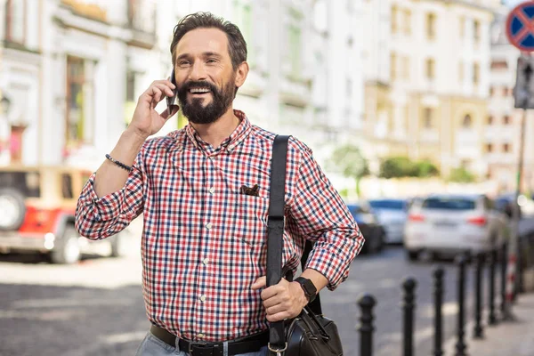 Glad to talk to you. Waist up of a cheerful delighted man talking on phone while walking along the street
