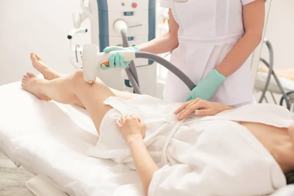 Close up photo of the medical worker standing close to the patient and removing vascular nets on her leg