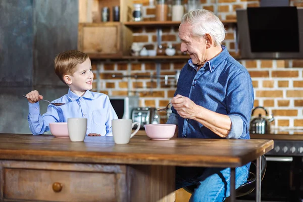 Alegre hombre mayor disfrutando de la comida con su nieto — Foto de Stock