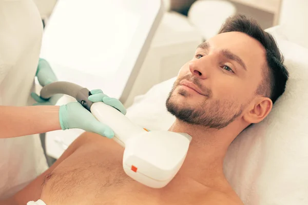 Lazer epilasyon prosedüründe boynuna yakın modern bir araç tutan lastik eldiven içinde sakin sakallı adam ve güzellik el yüzü