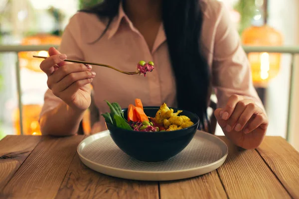 Close up photo of the lady in a pink blouse sitting at the table and taking her vegetarian meal on a fork
