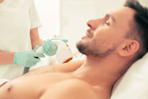Person in rubber gloves holding a modern tool while conducting laser hair removal with the patient