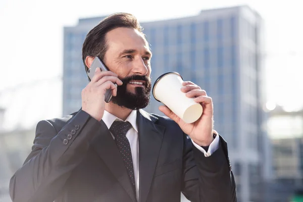 Call me back. Close up of a confident smiling businessman talking on phone while drinking morning coffee