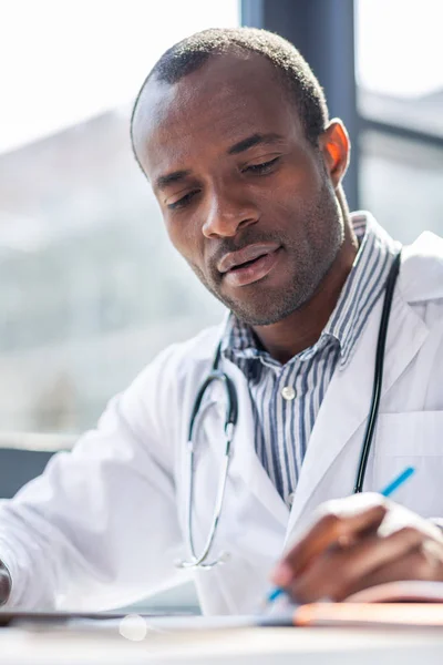 Medical study. Handsome international male bowing head while looking at his copybook