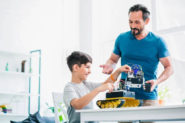 Mühendislik projesinde oğluna yardım ederken robot iktisadi bir cihaz tutan neşeli yetişkin adam