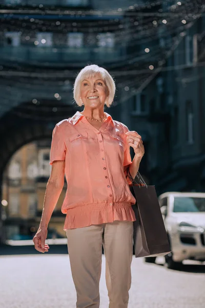 Happy pensioner walking in the street with paper bags and smiling