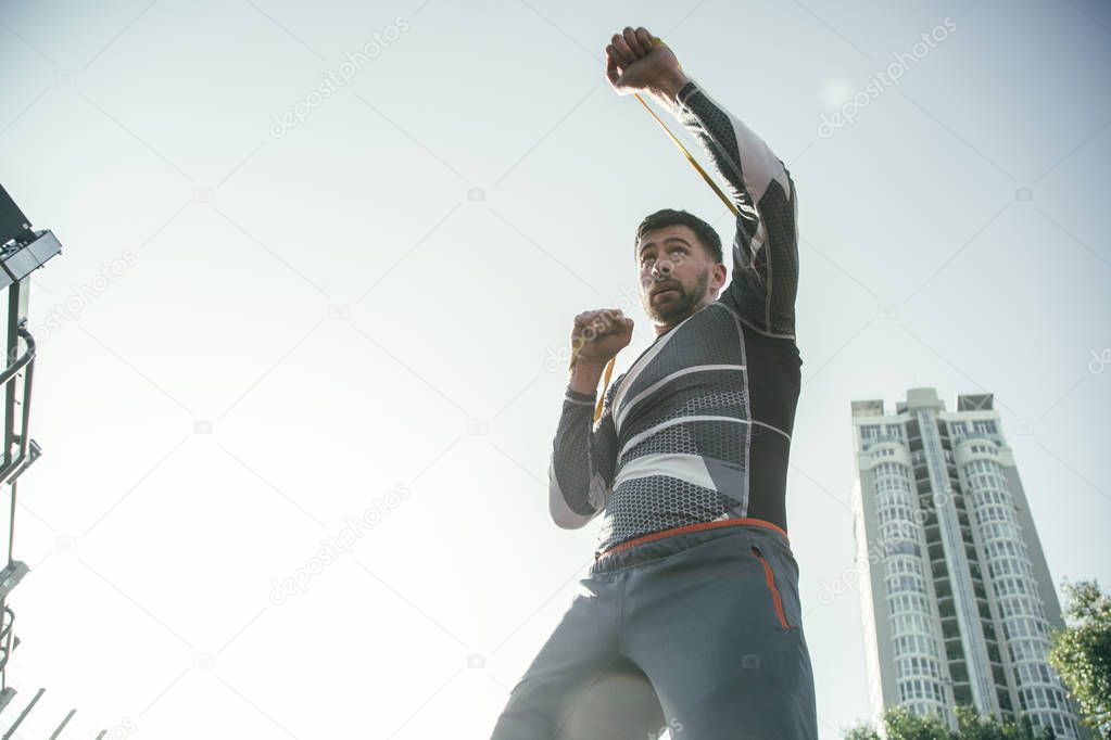 Attentive professional MMA boxer standing outdoors alone and having rubber rope on his fists while mastering punches