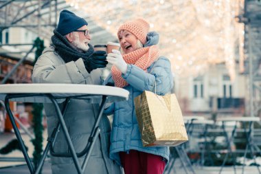 Yaşlı çift yeni yıl fuarında yuvarlak masanın yanında duran ve kağıt kahve fincanları clanging sırasında gülümseyerek