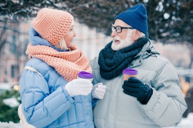 Karton bardakkahve ile ayakta ve gülümseyen yaşlı erkek ve kadın Keyifli konuşma
