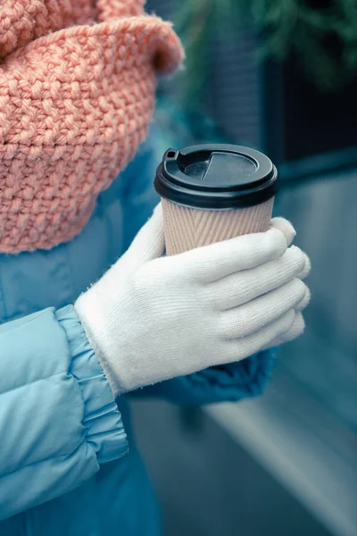 Close up photo of a carton cup of coffee. Person in warm gloves holding it