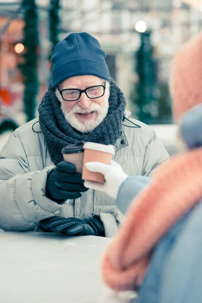 Sıcak giysiler içinde Pozitif yaşlı adam kış günü açık havada rahatlatıcı ve arkadaşı ile kahve bardak clanging