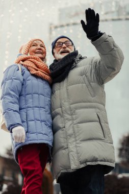 arka planda Noel aydınlatma ile sokakta duran ve gülümseyen kış kat olumlu emekliler kadar aist