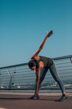 Sporcu köprüde açık havada ısınma yapıyor ve yere dokunuyor