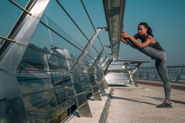 Sakin genç atlet köprü banister ayak koyarak ve bacak kasları germe