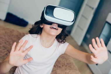 Gülümseyen kız evde sanal gerçeklik gözlüğü takarken ellerini öne uzatıyor ve onlara bakmaktan zevk alıyor.