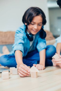 Neşeli çocuk evde yerde oturuyor ve bir binanın tahta parçalarıyla oynarken gülümsüyor.