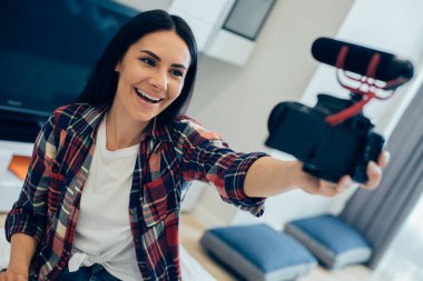 Tişörtlü neşeli kadın evde ve blog için kendini kameraya kaydetmenin tadını çıkarıyor.