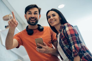 Akıllı telefonlu neşeli genç bir adam neşeli bir kadına bir şey gösteriyor ve parmağını işaret ediyor.