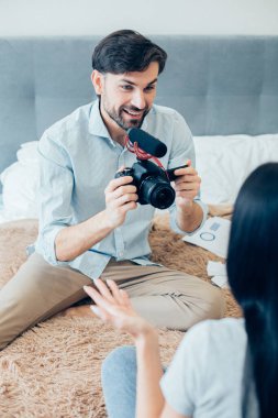 Yatakta kameralı ve mikrofonlu çekici bir adam otururken blogu için bir kadını kaydediyor.