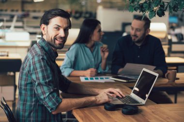 Modern bir dizüstü bilgisayarla masada oturan neşeli bir adam şirketin bir parçası olmanın sevincini dile getiriyor.