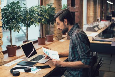 Dizüstü bilgisayarın önünde grafik çizelgeleriyle oturan ve dokunmatik ped kullanan sakin genç adam.