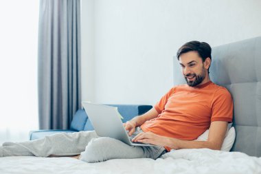 Mutlu bir yetişkin evde kalır ve gülümserken dizüstü bilgisayarla rahatça uzanır ve ekranına bakar.