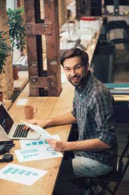 Mutlu genç adam gülümsüyor ve elini bilgisayarın klavyesine koyuyor.