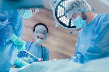 Ameliyathanede birlikte çalışan deneyimli cerrahlardan oluşan bir ekip. Üç doktorun konsantre yüzleri.