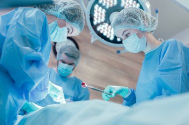 İki cerrah zor bir ameliyat yaparken kadın doktor pense pamuk tutuyordu.