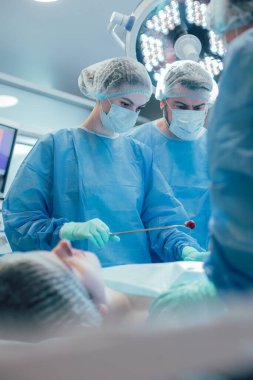 Ameliyathanede bir hastanın midesine bakarken kaşlarını çatan endişeli bir doktor. Forseps giymiş pamuklu bir kadın doktor.
