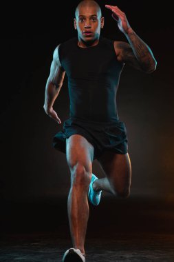 Şortlu ve tişörtlü kararlı sporcu hızlı koşuyor ve mesafeye bakıyor.