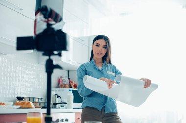 Kareli gömlekli güzel bayan blogu için video kaydederken kameraya bakıyor.