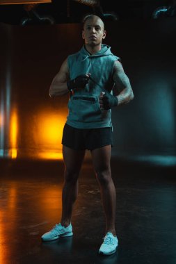 Sportif giysiler içindeki kendine güvenen sporcu mesafeye bakıyor ve boks bandajını eline sarıyor.