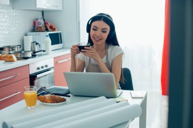 Pozitif tasarımcı uzak işinden dinleniyor ve dizüstü bilgisayarının önünde bir fincan kahveyle otururken gülümsüyor.