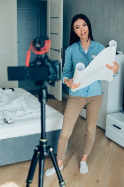 Sakin akıllı kadın yatak odasında kameranın önünde duruyor ve elinde bir rulo kağıt var.