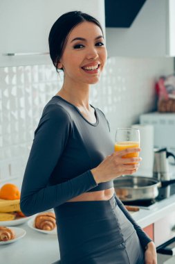 Evde otururken gülümseyen ve bir bardak meyve suyu içen güzel bir kadın.
