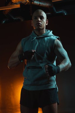 Ciddi kararlı dövüşçü boks bandajı ile ayakta duruyor ve başka tarafa bakarken onu bileğine bağlıyor.