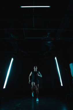 Ciddi, cesur, kaslı bir adam karanlık bir stüdyoda iki yumuşak kutunun ışığı arasında koşuyor.