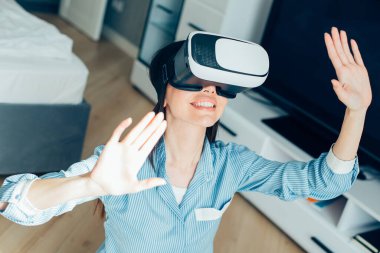 Modern sanal gerçeklik cihazını takarken gülümseyen ve ellerini kaldıran olumlu beyaz kadın.