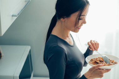 Güzel bayan mutfakta elinde bir kase mısır gevreği ve elinde kaşıkla gülümsüyor.